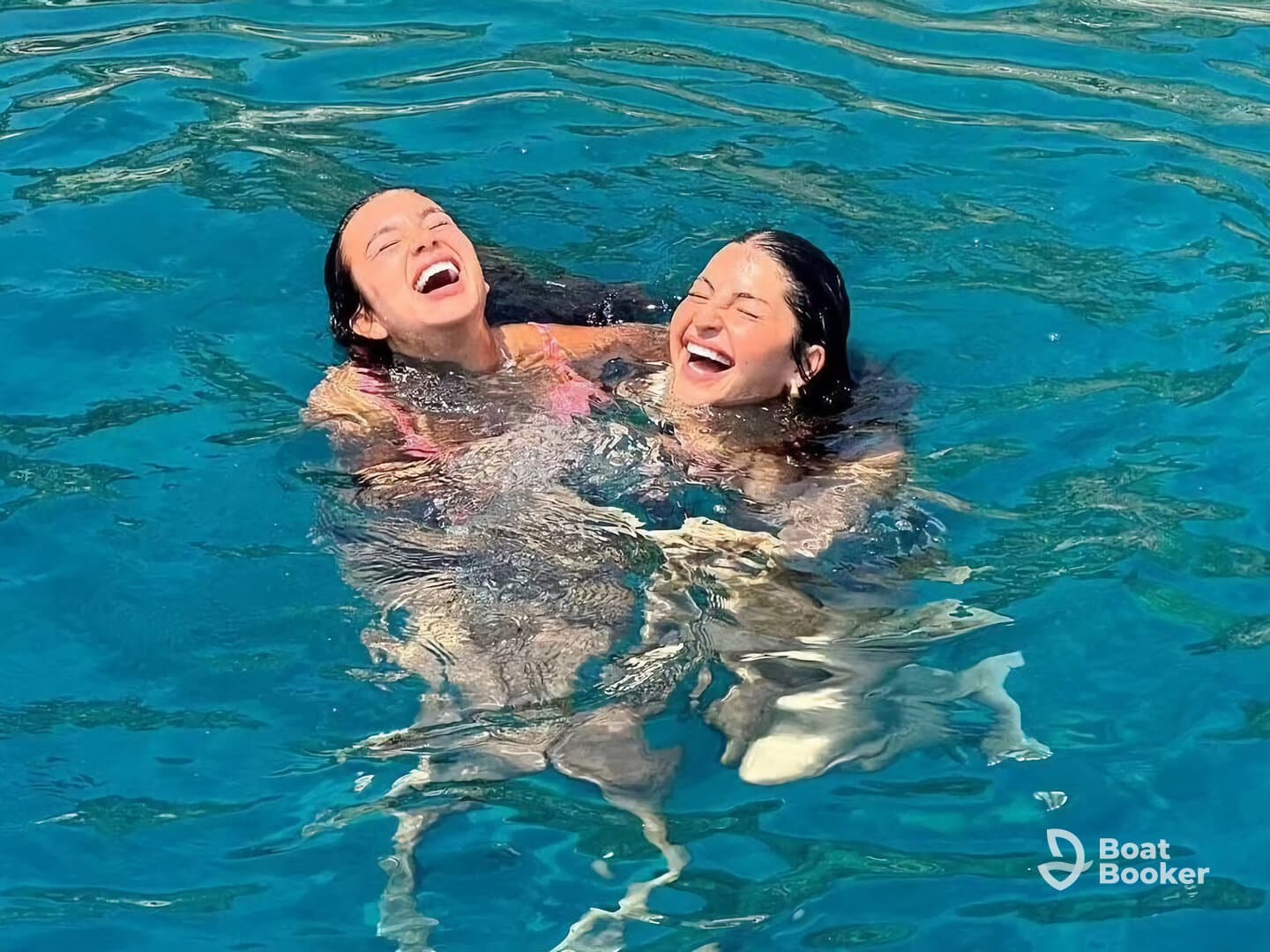Two friends share a joyful moment while swimming in crystal-clear waters, capturing the essence of fun and adventure on a boating trip.