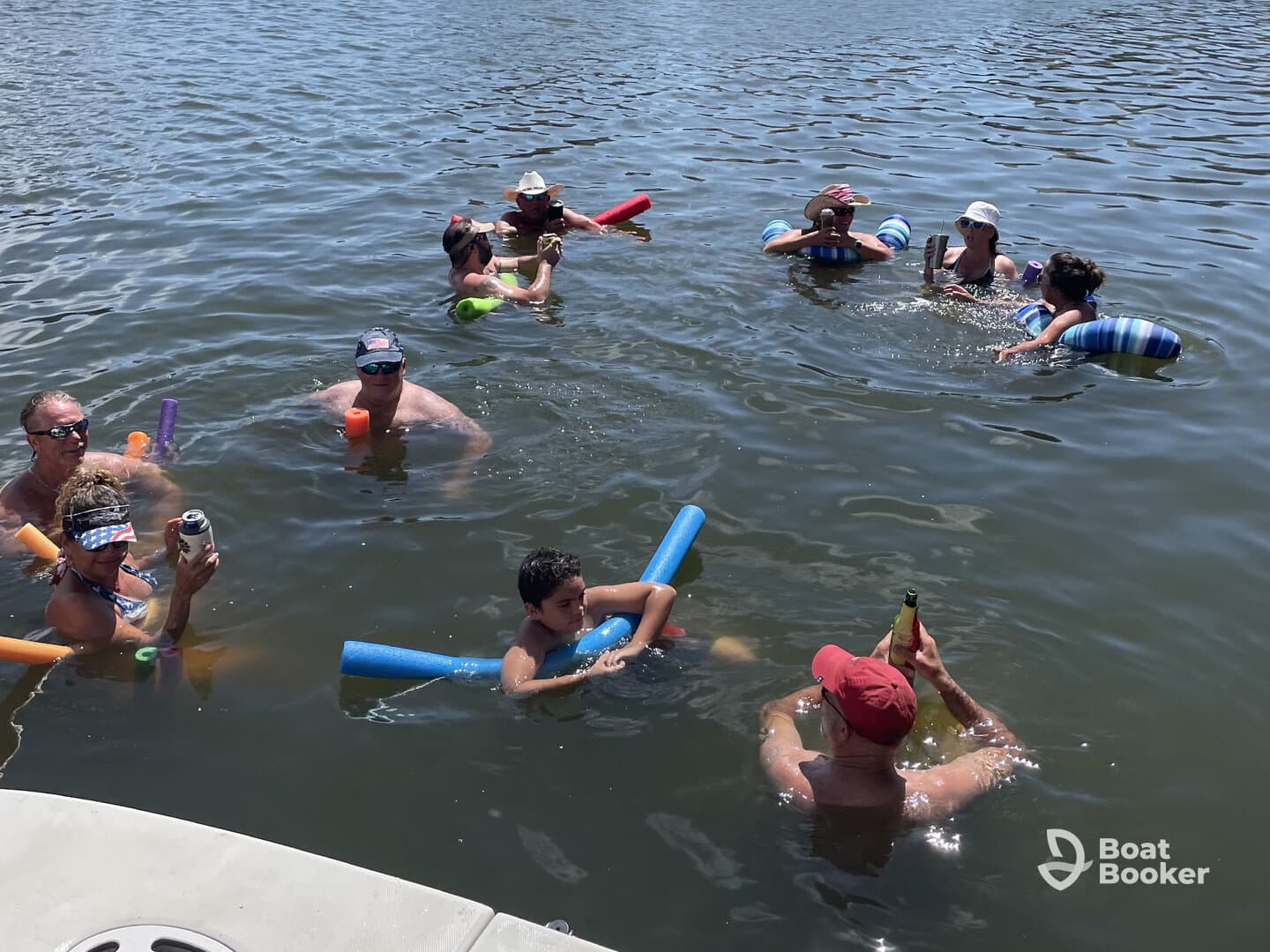 A lively group enjoys a fun day in the water, complete with pool noodles and drinks, making for a perfect summer party atmosphere.