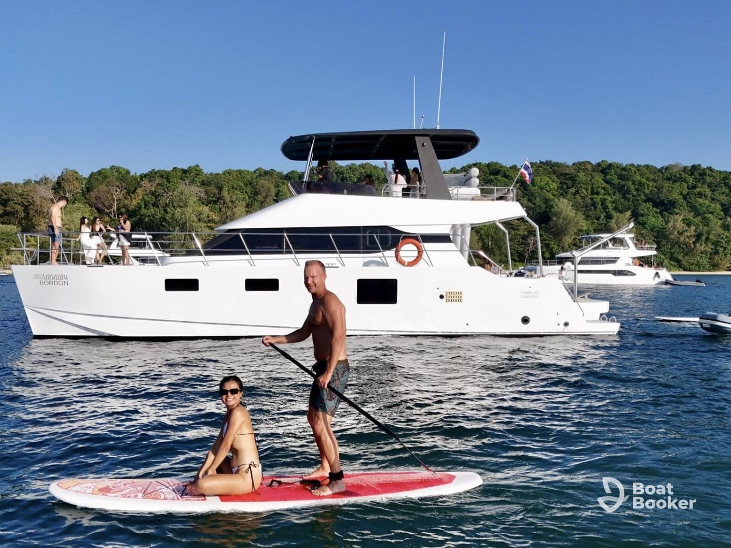 A couple enjoys paddleboarding in front of a luxurious yacht, capturing the essence of fun-filled water activities and relaxation on the water.