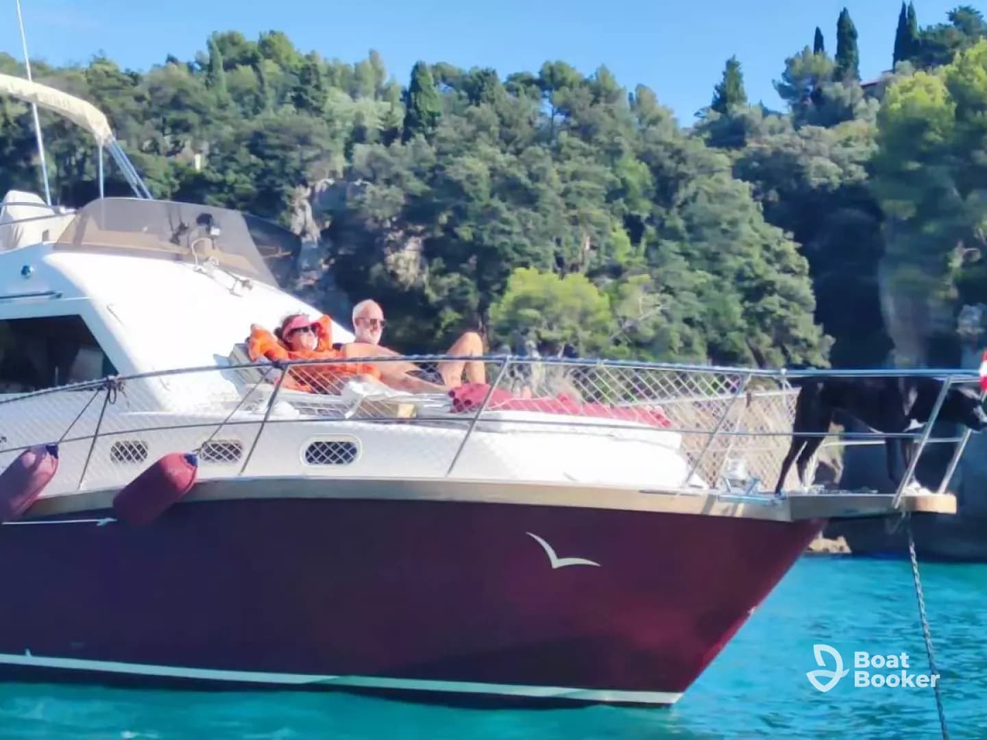 A couple relaxes on the deck of their boat, enjoying the sun and the beautiful surroundings, with a dog also enjoying the moment — a perfect day on the water.