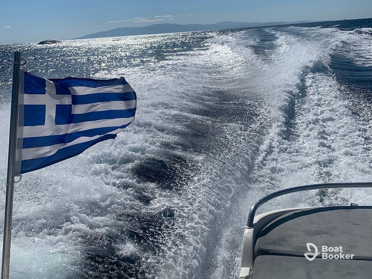 A stunning view of a boat cutting through the sparkling waters of Greece, with the national flag waving proudly in the breeze.