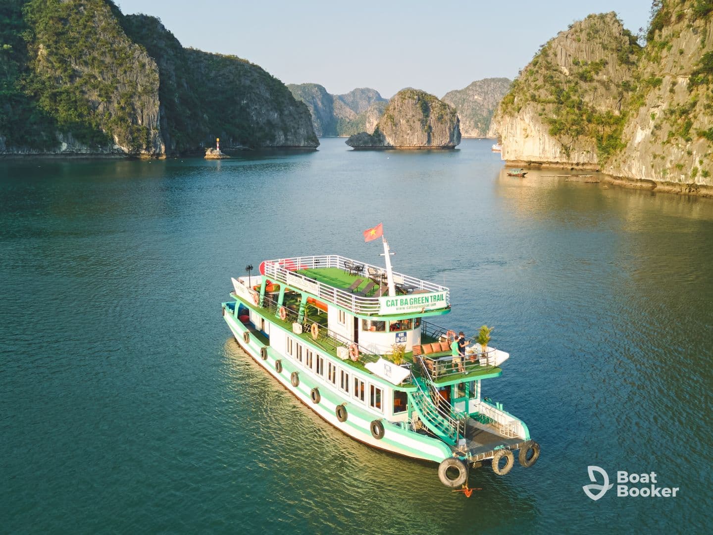 A vibrant boat named 'Cat Ba Green Trail' navigates through stunning limestone karsts in a serene bay, showcasing the beauty of the landscape and the vessel.