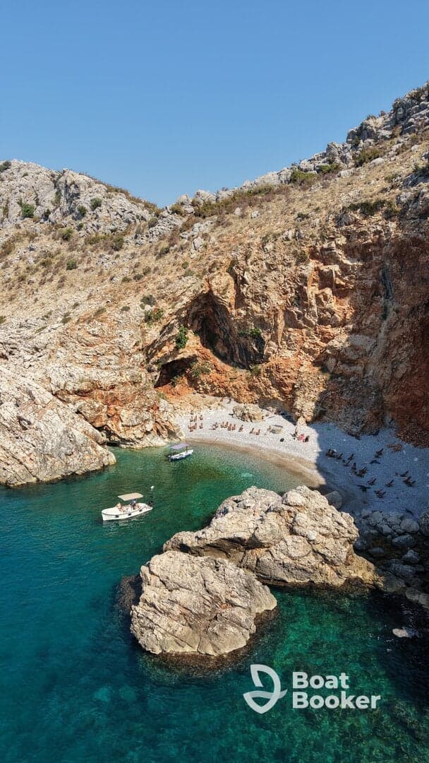 A stunning aerial view of a secluded beach with sunbathers enjoying the sun, complemented by a small boat anchored nearby — a perfect getaway for relaxation and coastal exploration.