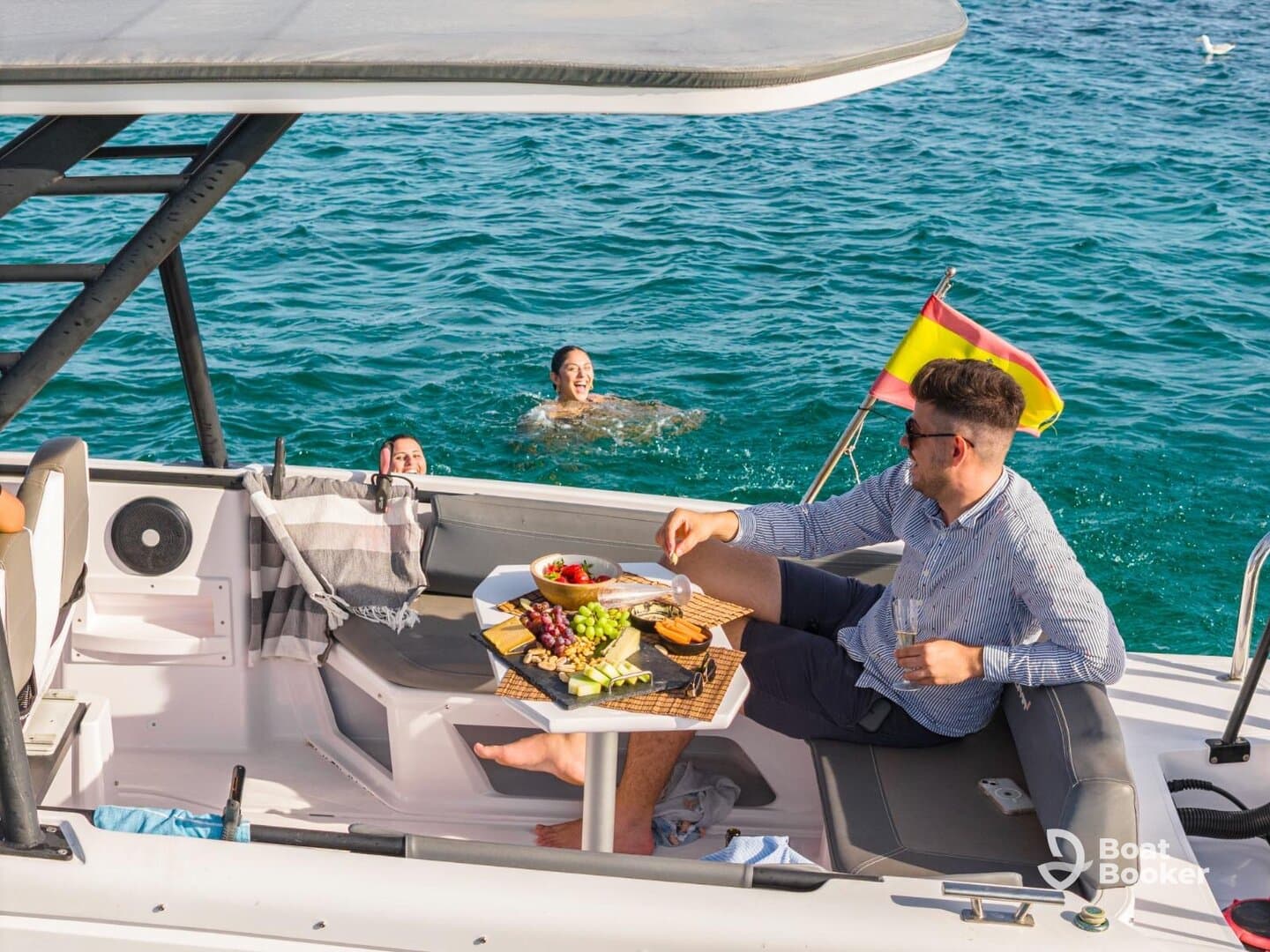 A lively scene on a pontoon boat with friends enjoying a delicious spread of food and drinks while others swim in the clear waters — perfect for a fun day on the water.
