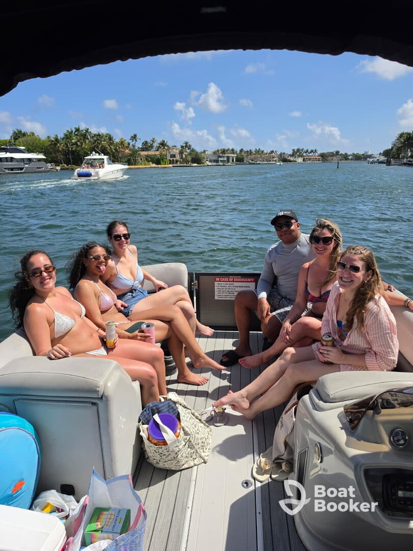 A lively group of friends enjoys a sunny day on a pontoon boat, sipping drinks and soaking up the sun — perfect for a fun day on the water.