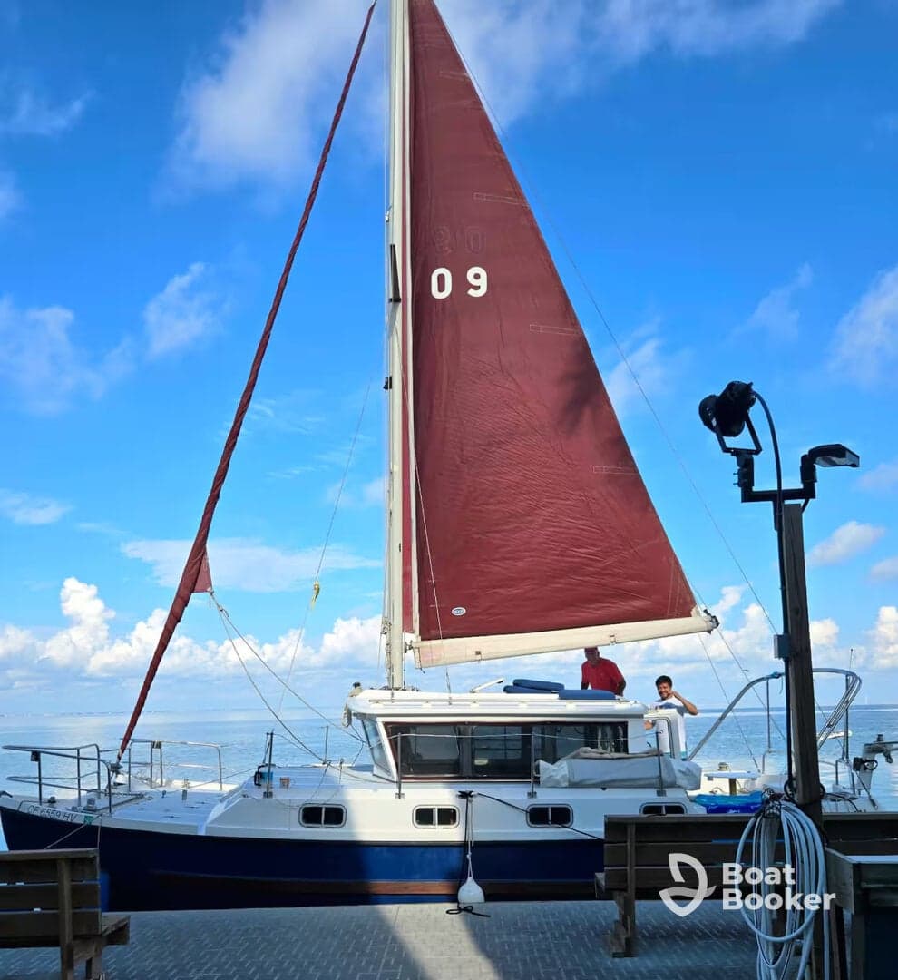A vibrant sailboat is docked with two individuals on board, set against a stunning blue sky — perfect for sailing adventures and exploring the open waters.