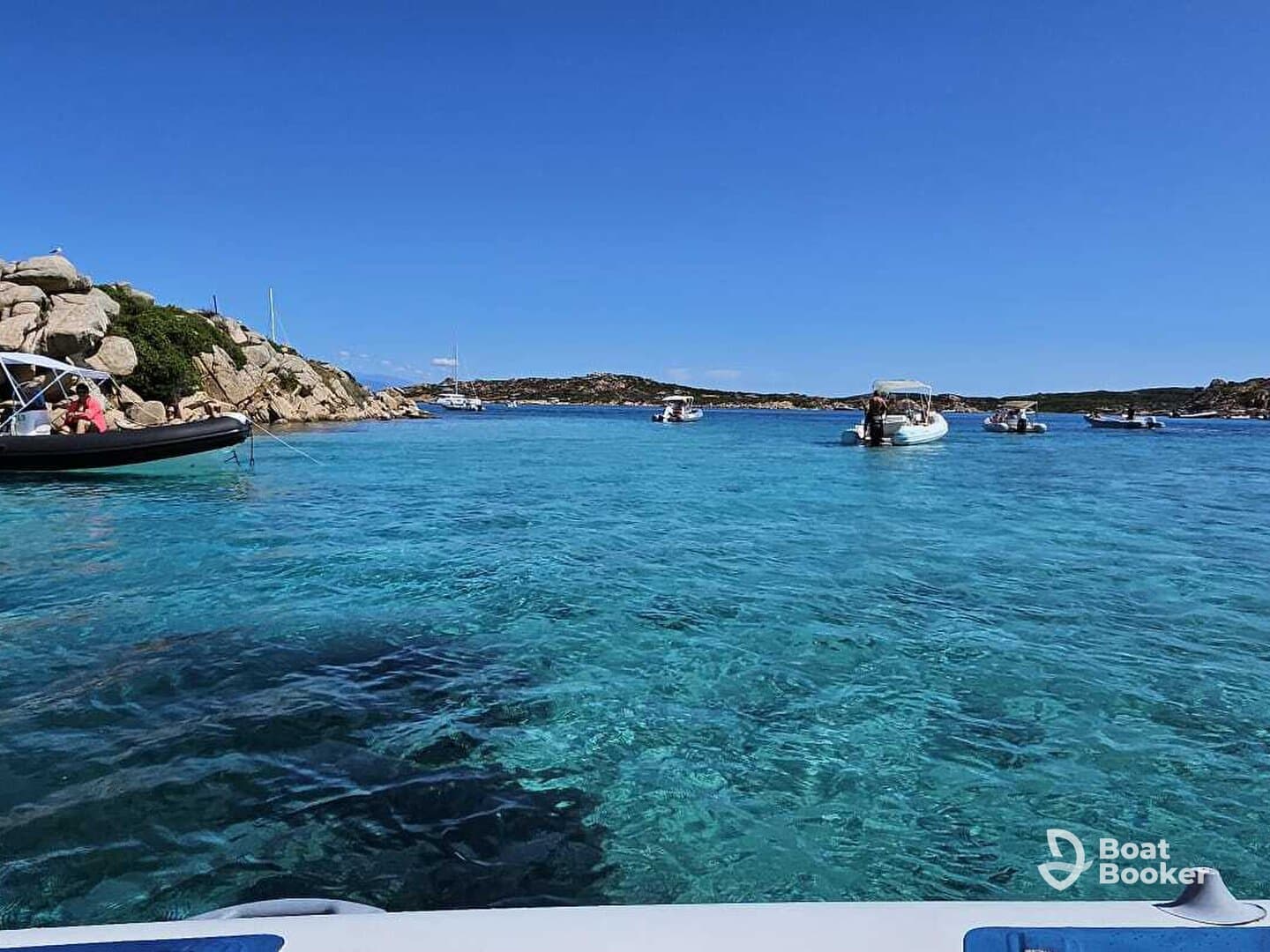 A picturesque view of several boats anchored in crystal-clear turquoise waters near a rocky coastline, showcasing the beauty of a perfect day on the water.