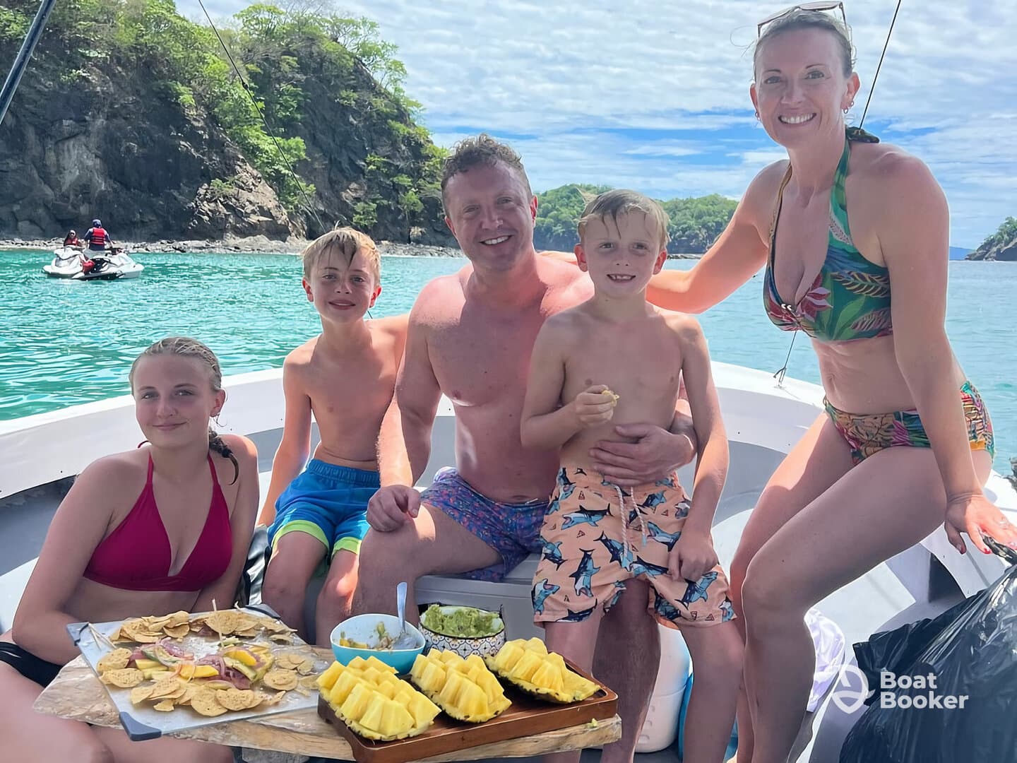 A joyful family enjoys snacks aboard a boat, surrounded by stunning turquoise waters — perfect for a fun day out on the water.