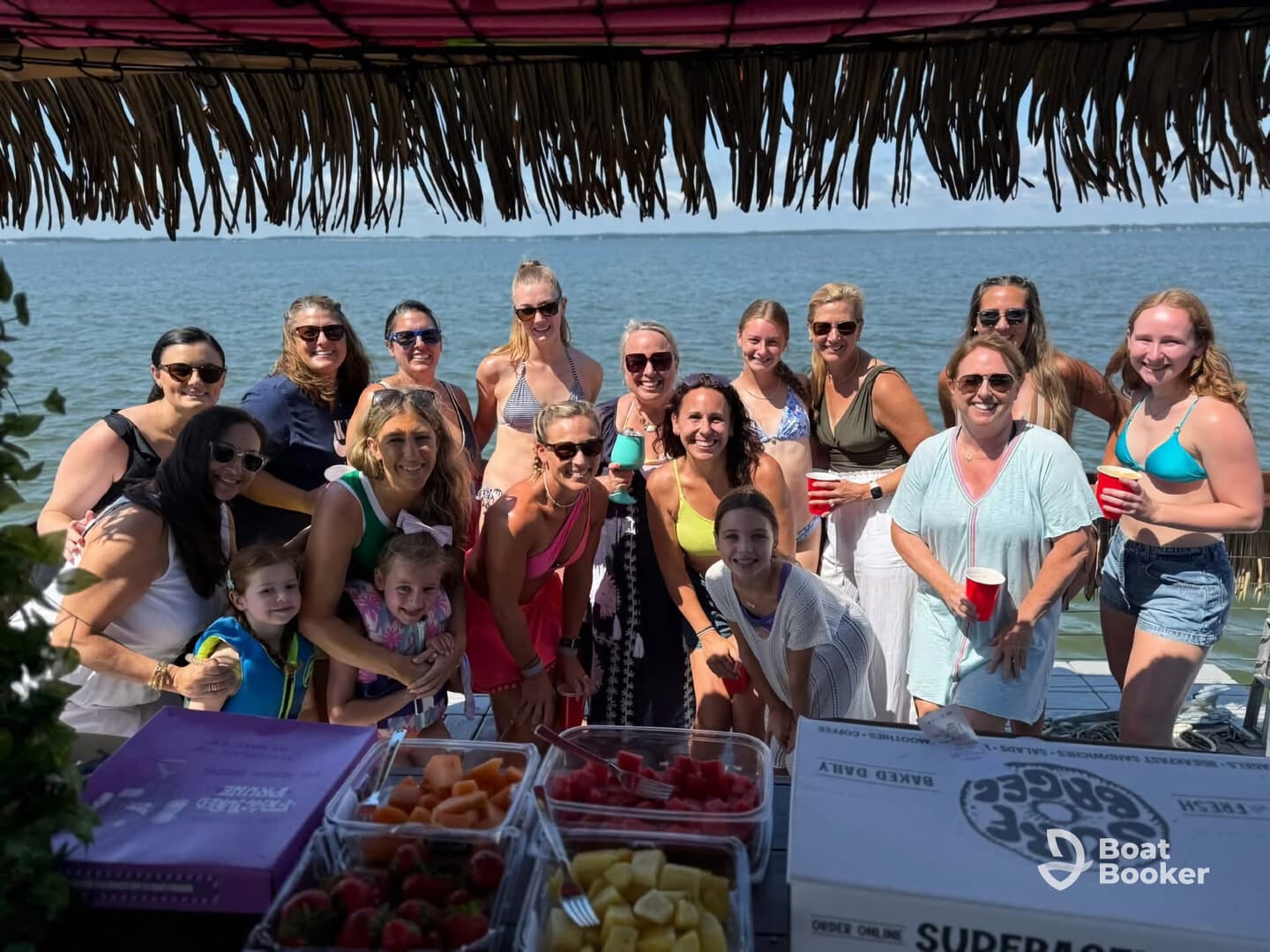 A lively group of friends celebrates together on a boat, enjoying food and drinks while soaking up the sun — perfect for a fun day on the water.