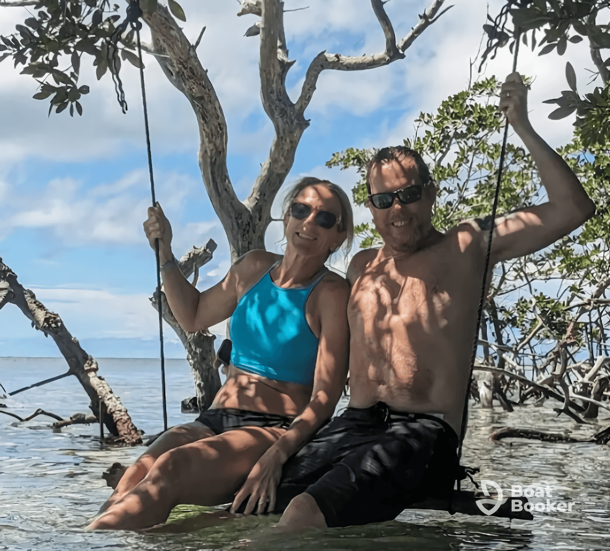 A couple enjoys a playful moment swinging in shallow waters surrounded by mangroves, capturing the essence of a fun day on the water.