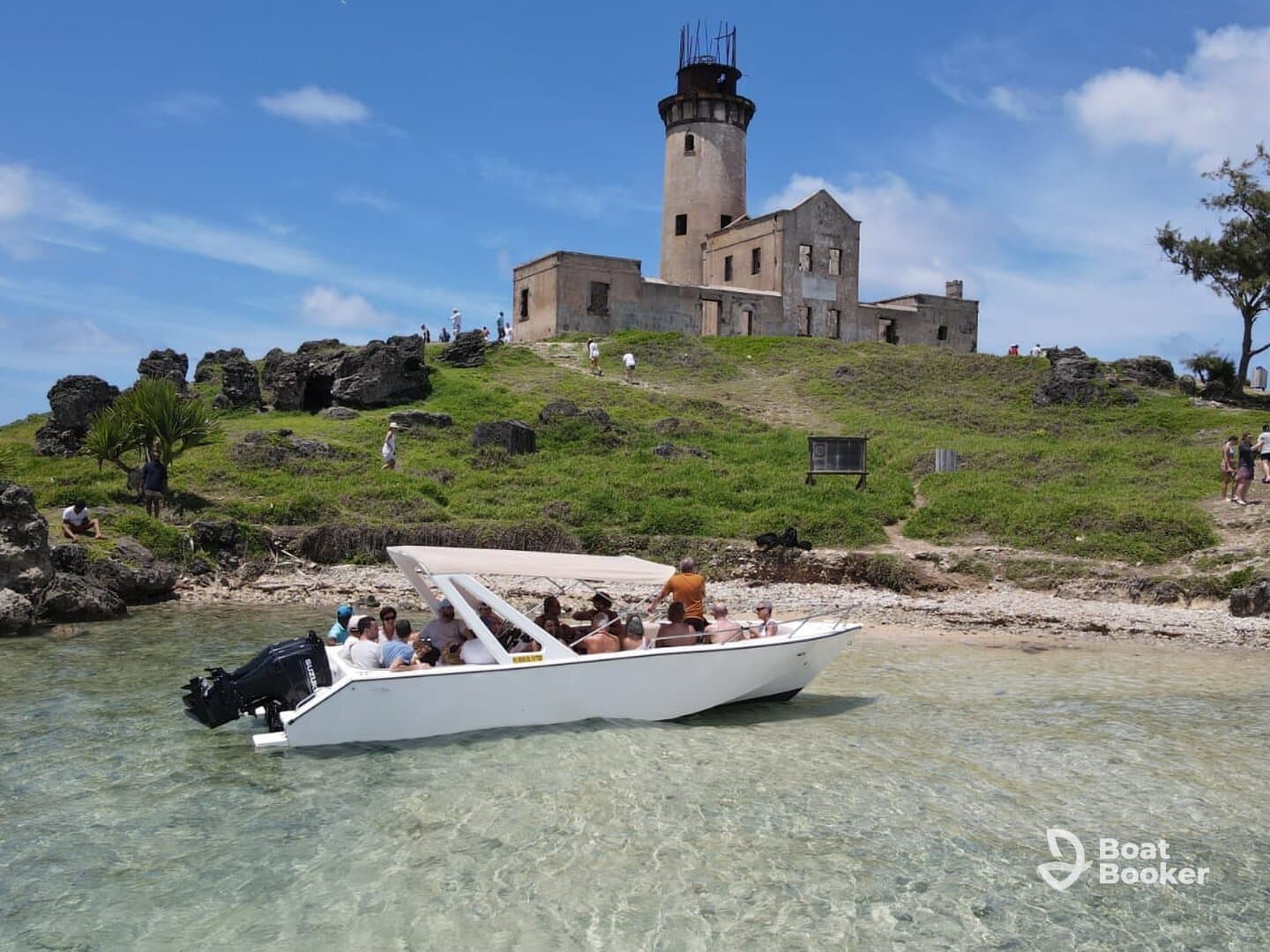 A lively group enjoys a beach stop aboard a boat, with a historic lighthouse in the backdrop — perfect for exploration and adventure on the water.
