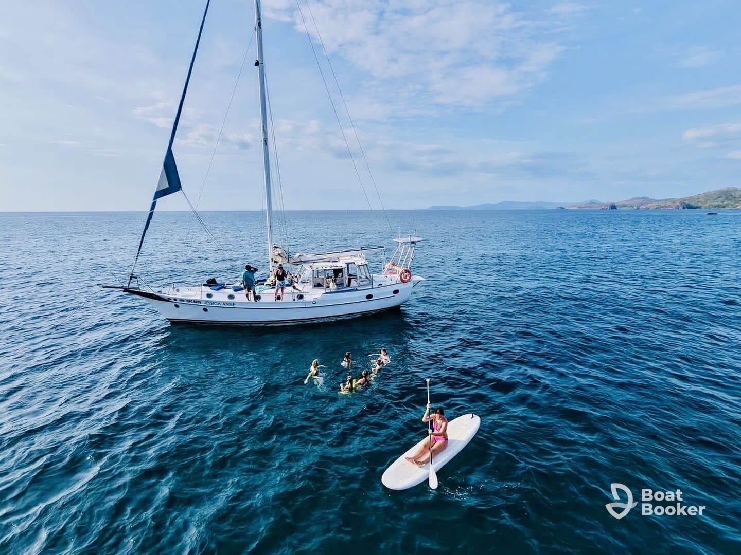 A vibrant scene of guests enjoying snorkeling and paddleboarding near a sailboat, showcasing the fun and adventure of a day on the water.
