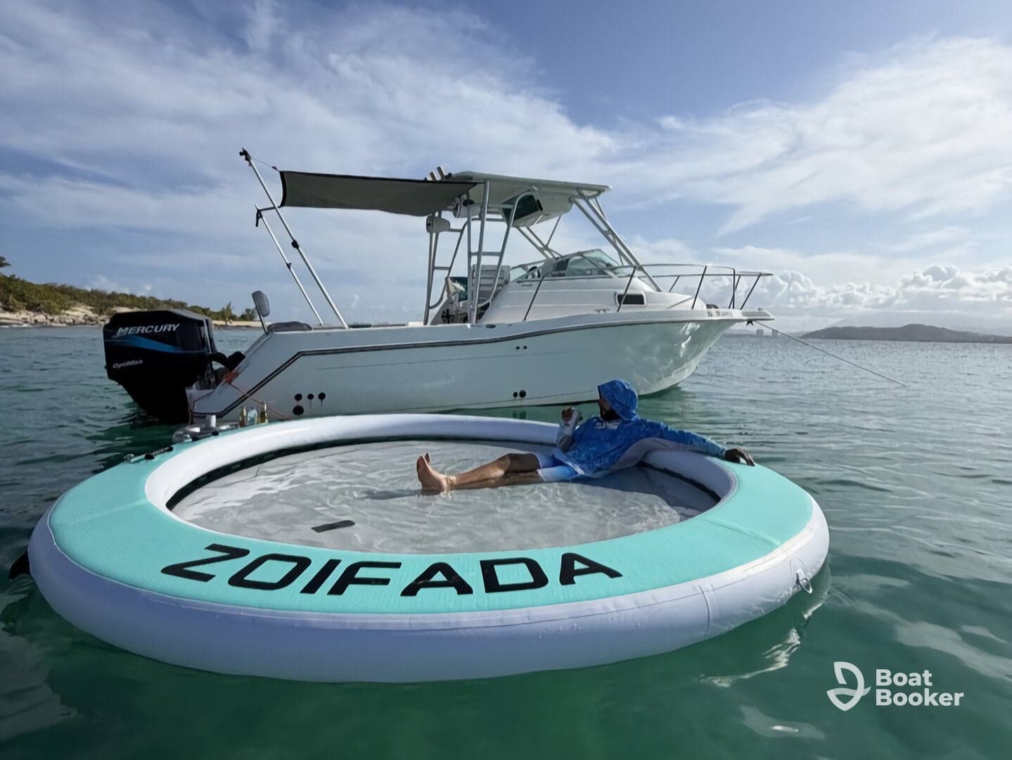 A person relaxes on a floating mat in clear waters next to a boat, enjoying a sunny day on the water — perfect for leisure and fun activities.
