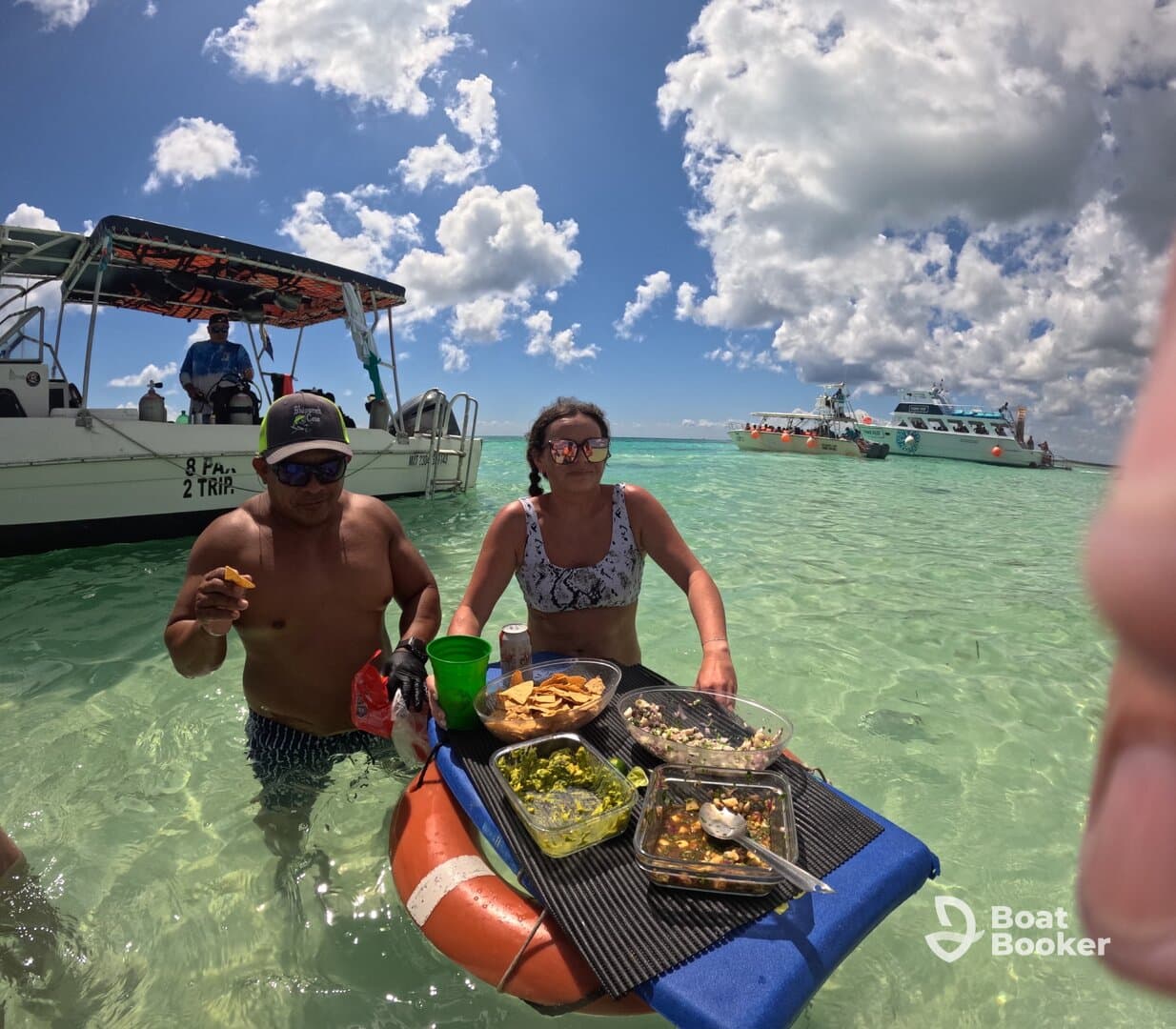 Guests enjoy delicious snacks while wading in clear waters, with boats in the background — a perfect setting for a fun day on the water.