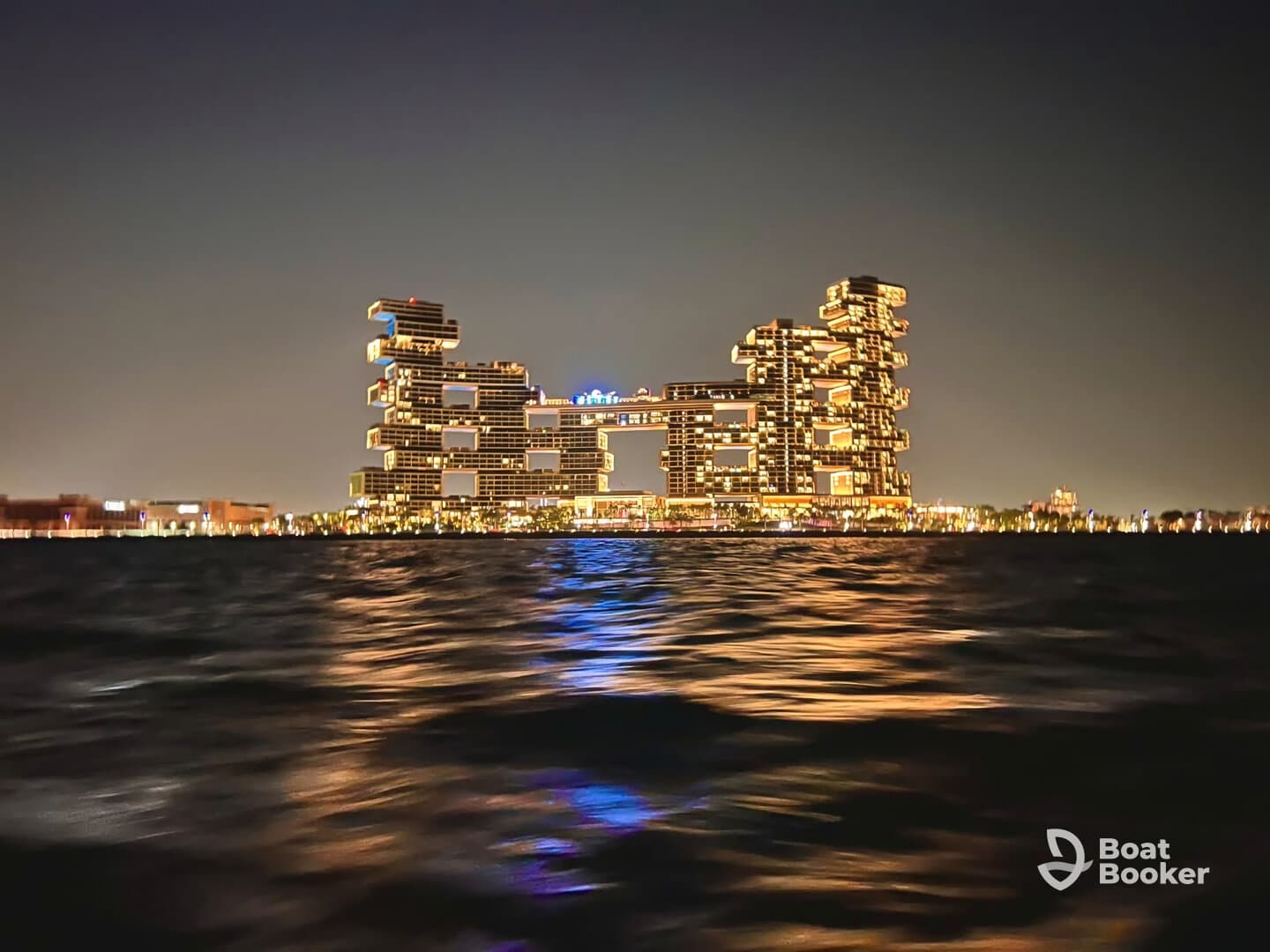 A nighttime view of a uniquely designed building reflecting lights on the water, creating an atmospheric scene.