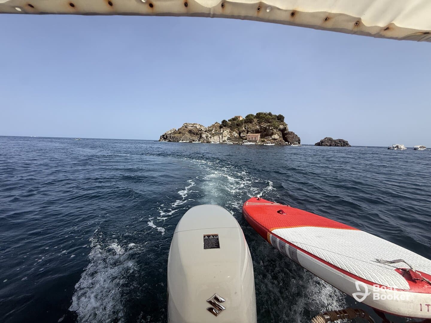 A scenic view of a boat heading towards a picturesque island, with a paddleboard visible at the side — perfect for exploring the beautiful waters and enjoying water activities.