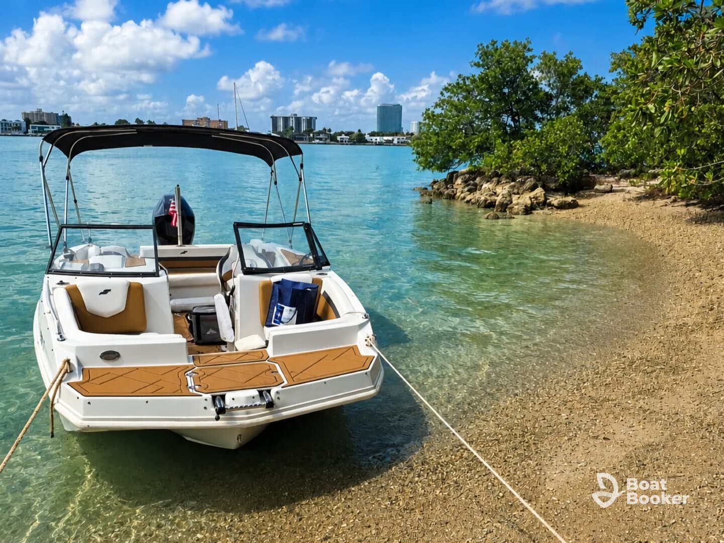 A sleek boat is anchored near a sandy shore, showcasing its elegant design against a backdrop of clear blue waters and lush greenery.