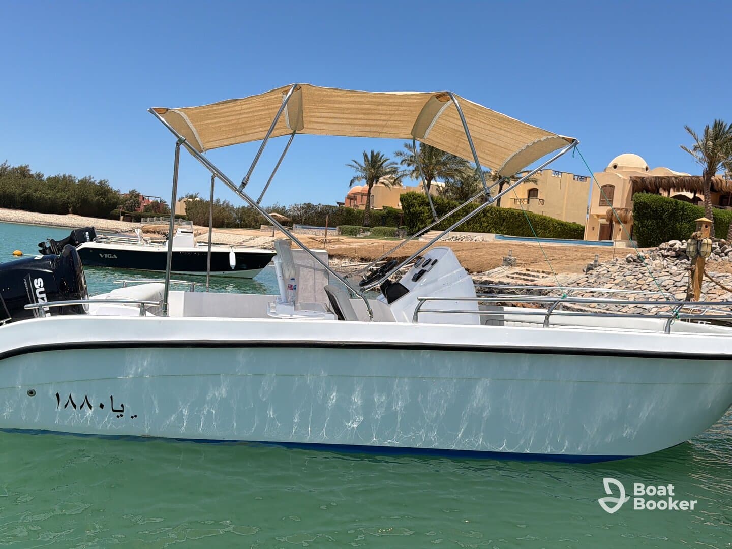A sleek boat with a canopy is docked in calm waters, showcasing its design against a picturesque backdrop of palm trees and sandy shores.