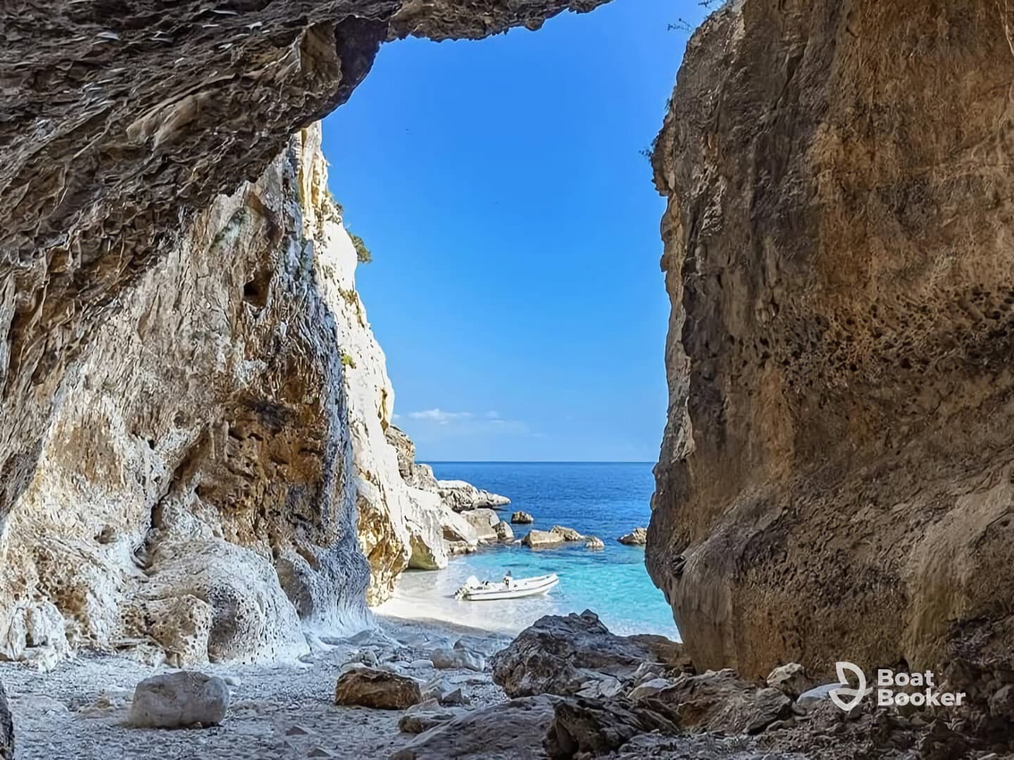 A stunning view from inside a cave overlooking a tranquil beach and a small boat anchored in the clear blue waters — a perfect destination for exploration and relaxation.