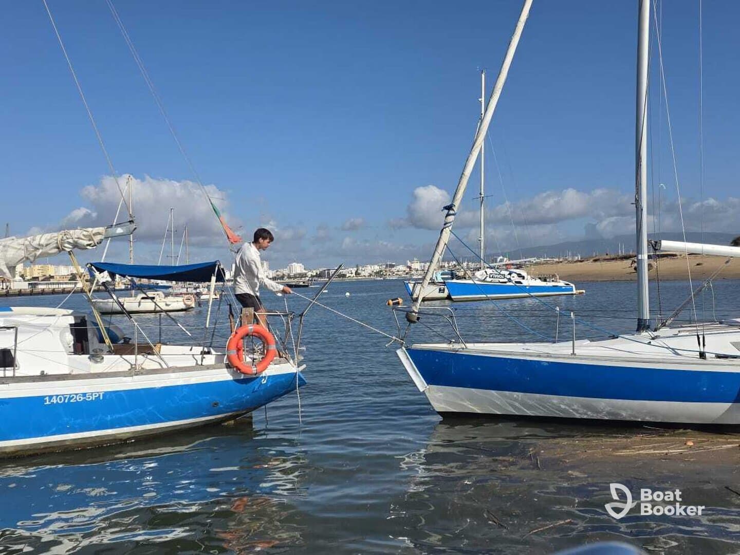 A sailor prepares to fish from the deck of a boat in a picturesque harbor, showcasing the joy of sailing and water activities.