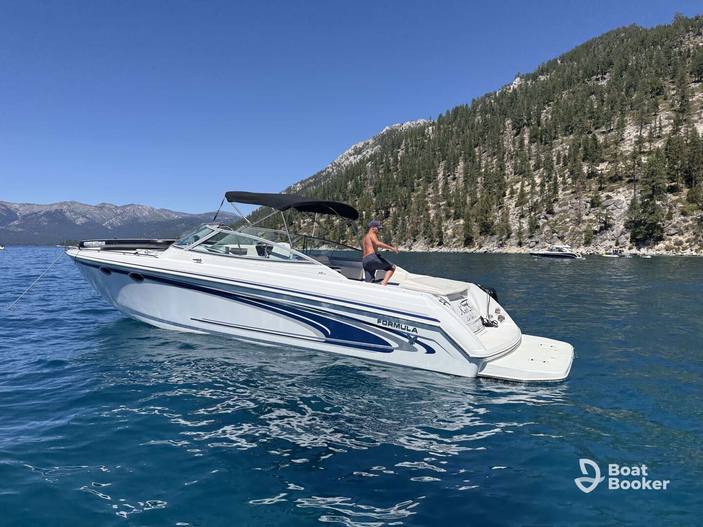 A man enjoys a sunny day on a sleek boat at the lake, surrounded by stunning mountain scenery — perfect for summer adventures on the water.