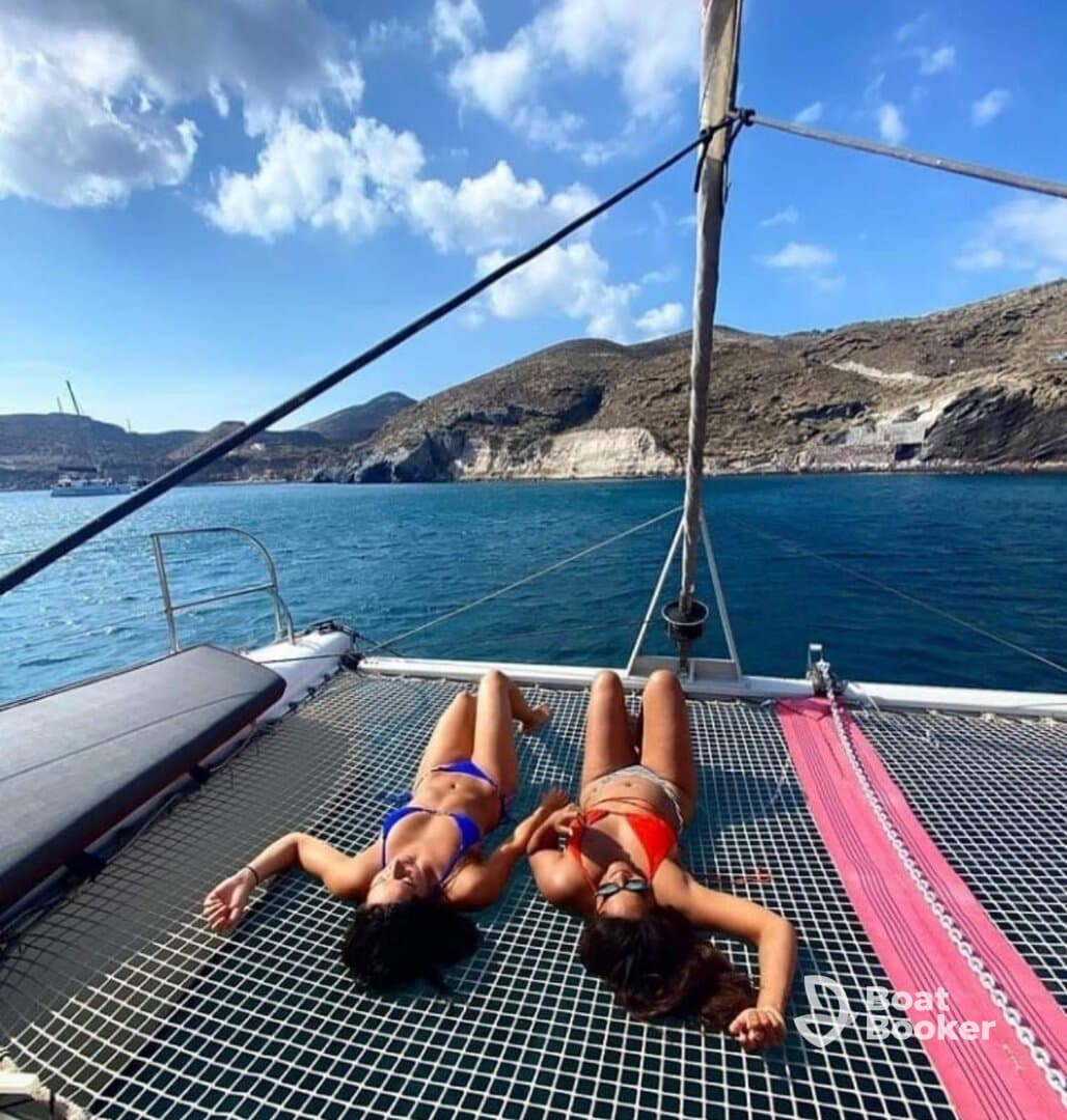 Two friends relax and sunbathe on the netting of a catamaran, enjoying the beautiful ocean view and perfect weather — an ideal moment for relaxation on the water.