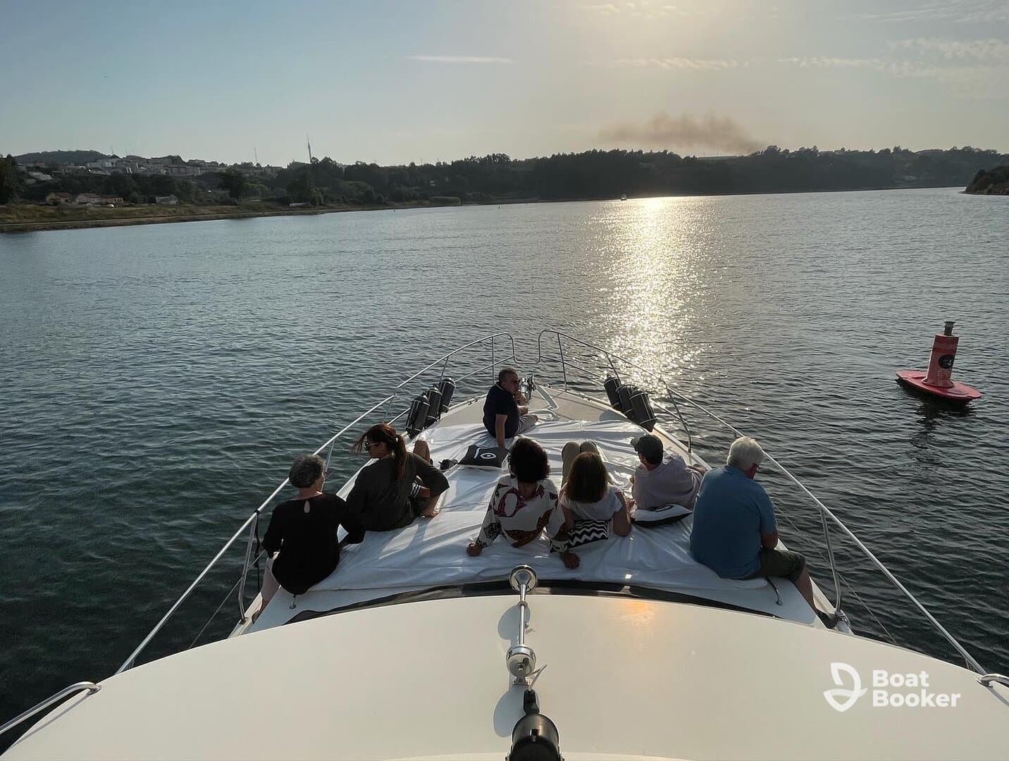A group of friends enjoys a relaxing moment on the bow of a boat, surrounded by serene waters and a beautiful sunset backdrop.