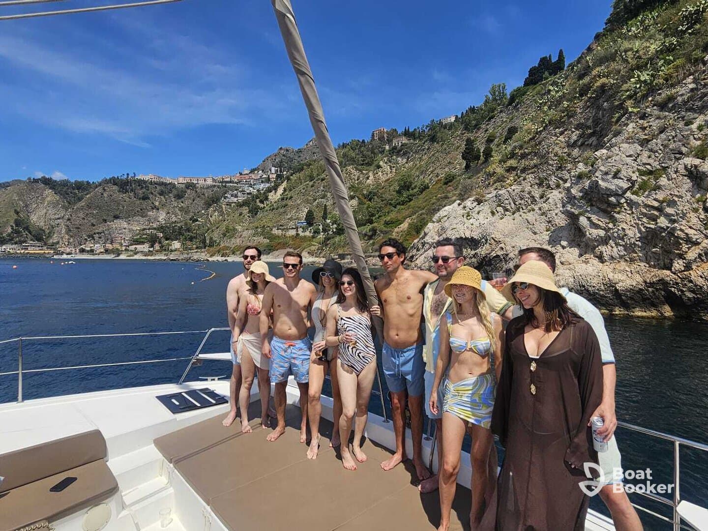 A lively group enjoys a sunny day on a yacht, showcasing the perfect atmosphere for celebration and relaxation against a stunning coastal backdrop.