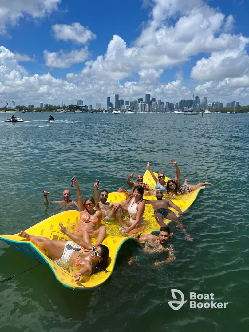 A lively group enjoys a fun day on a floating mat in the water, with the stunning Miami skyline in the background — perfect for summer celebrations and group outings.