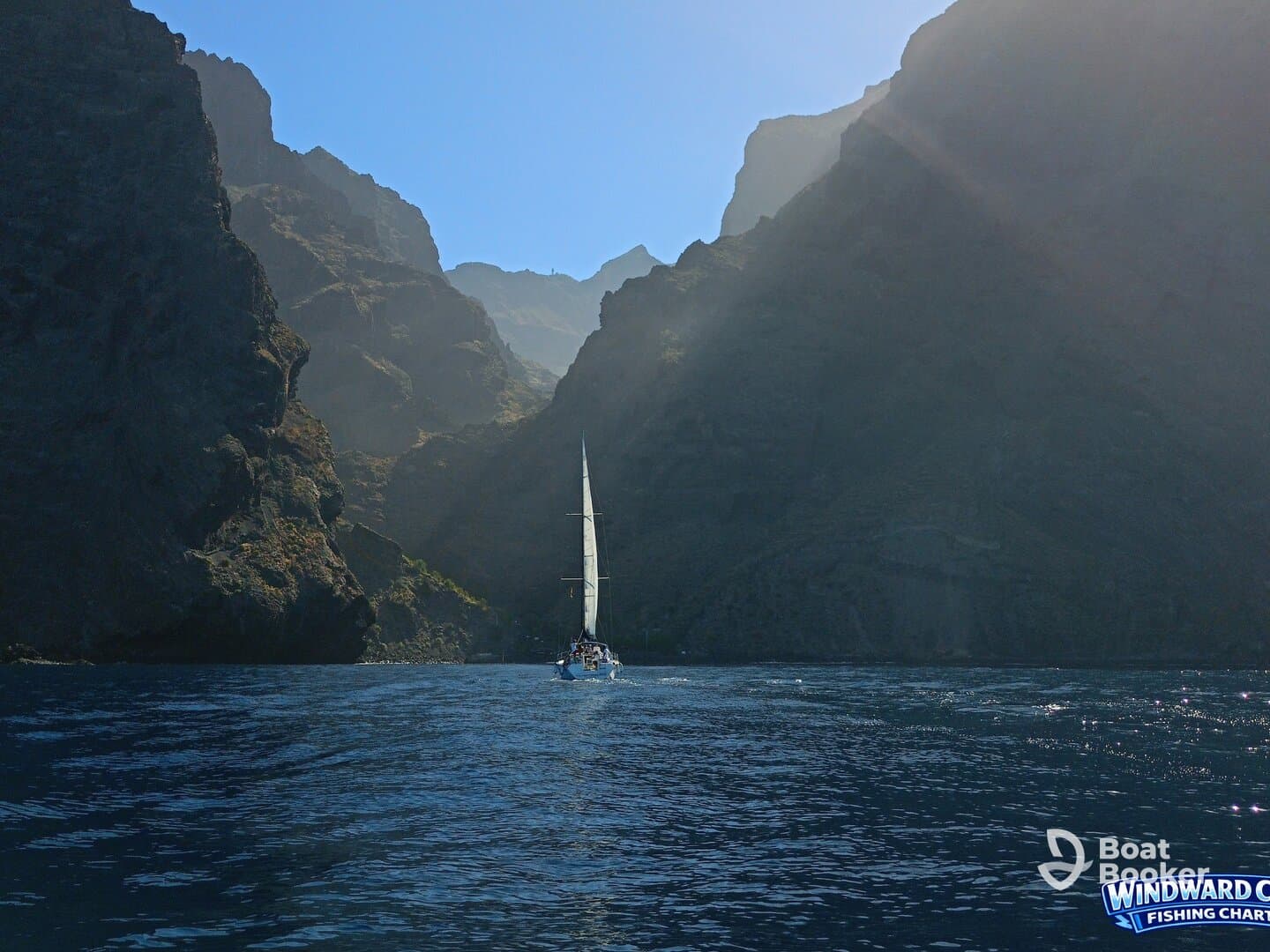 A sailboat navigates through a stunning coastal canyon, showcasing the breathtaking scenery of the surrounding cliffs and ocean — a perfect backdrop for sailing adventures.