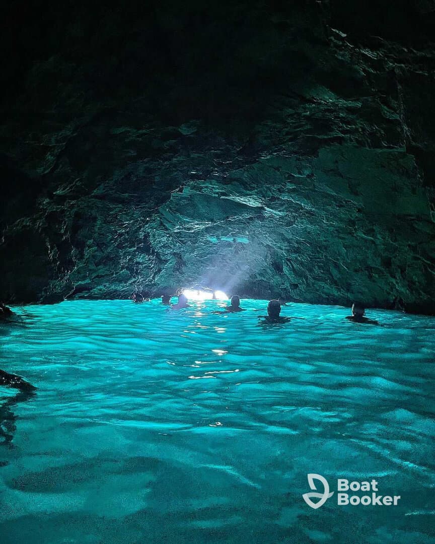 A group of swimmers enjoys the stunning turquoise waters inside a cave, illuminated by natural light — a breathtaking adventure in a unique underwater setting.