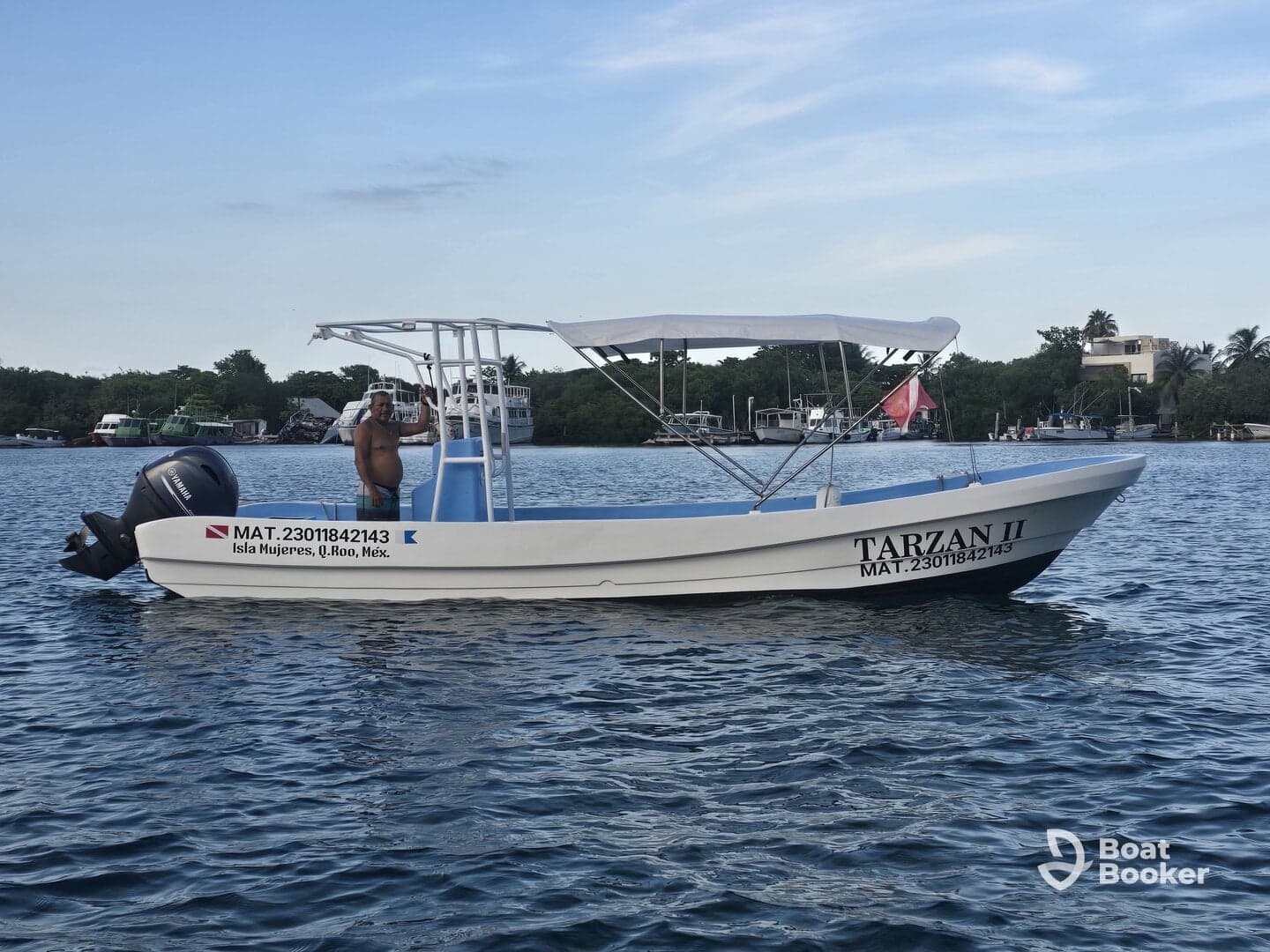 A man waves from the deck of the 'Tarzan II' boat in Isla Mujeres, showcasing the vibrant marine life and scenic views of the area.