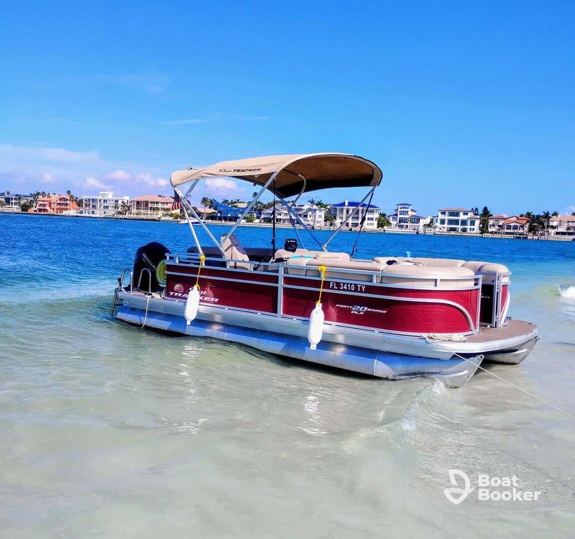 A vibrant pontoon boat is docked in clear waters, showcasing its spacious design against a picturesque waterfront backdrop.