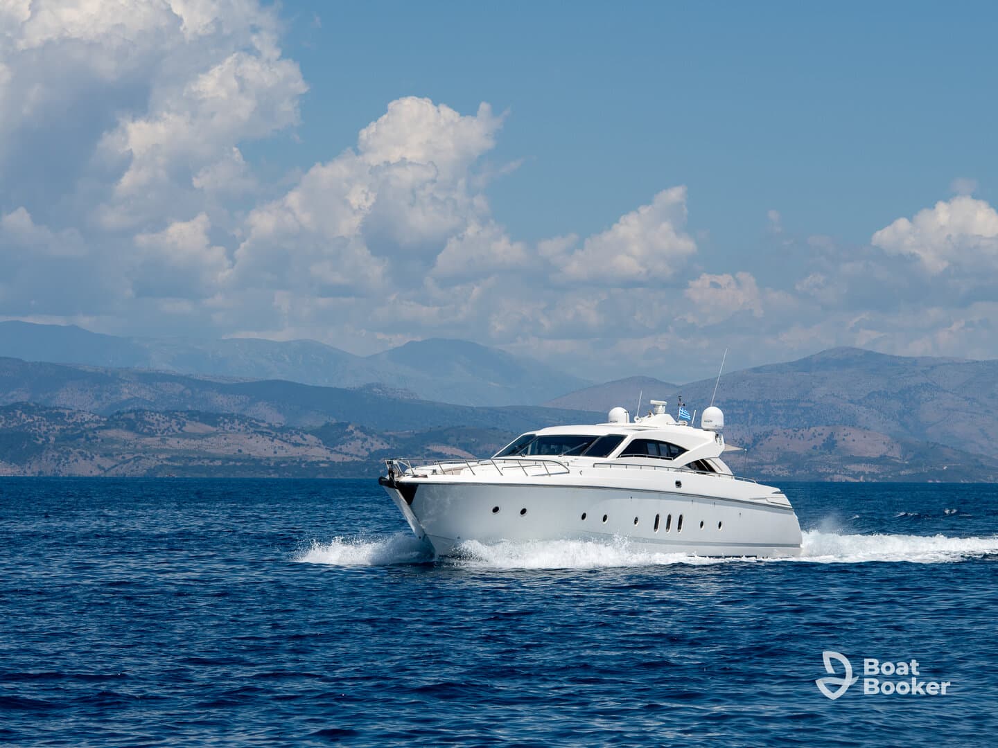 A sleek yacht cruises through the sparkling blue waters, showcasing its elegant design against a backdrop of mountains and fluffy clouds.