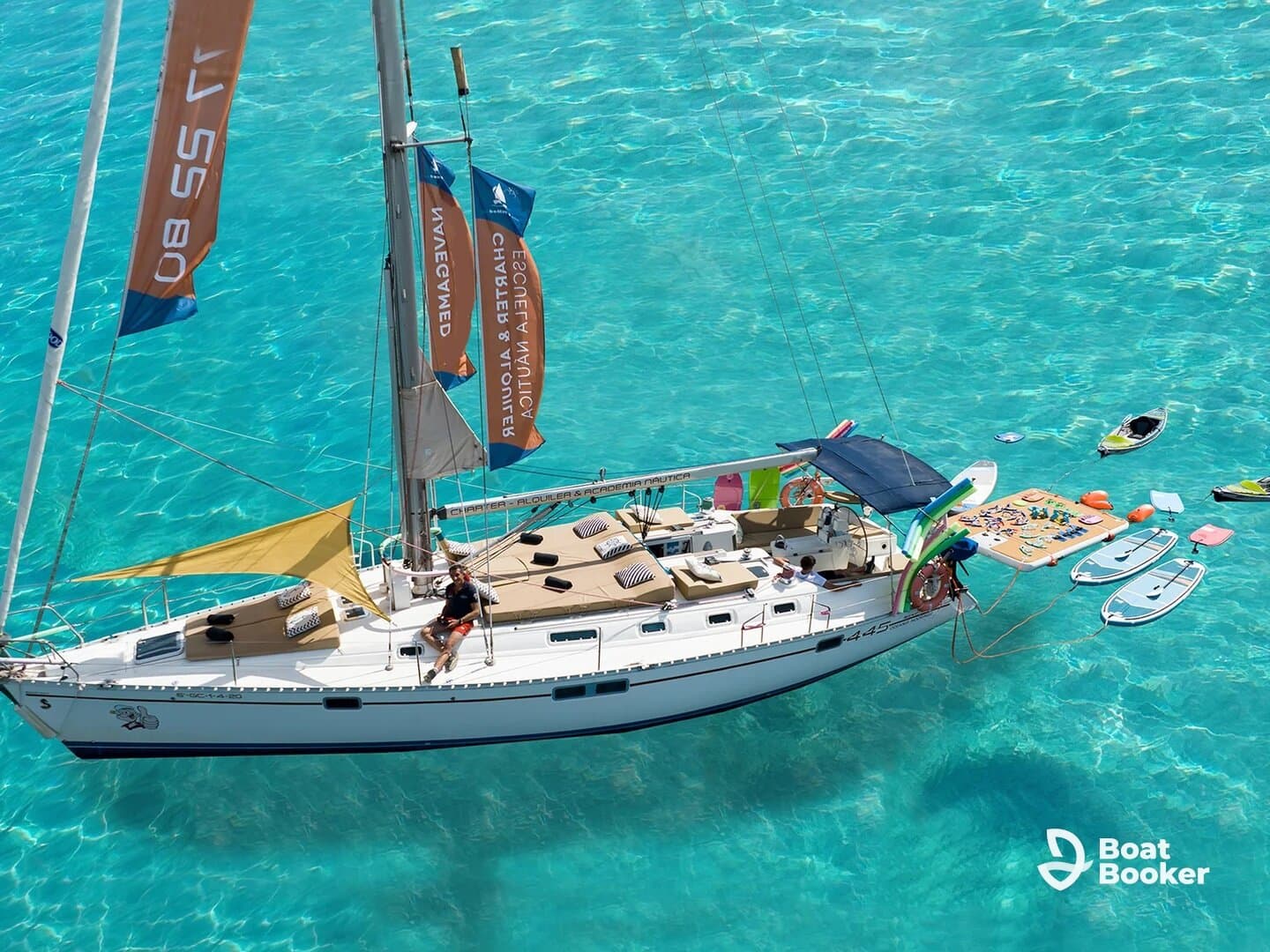 An aerial view of a vibrant sailboat anchored in crystal-clear waters, featuring guests enjoying paddleboarding and snorkeling gear — a perfect scene for water adventures.
