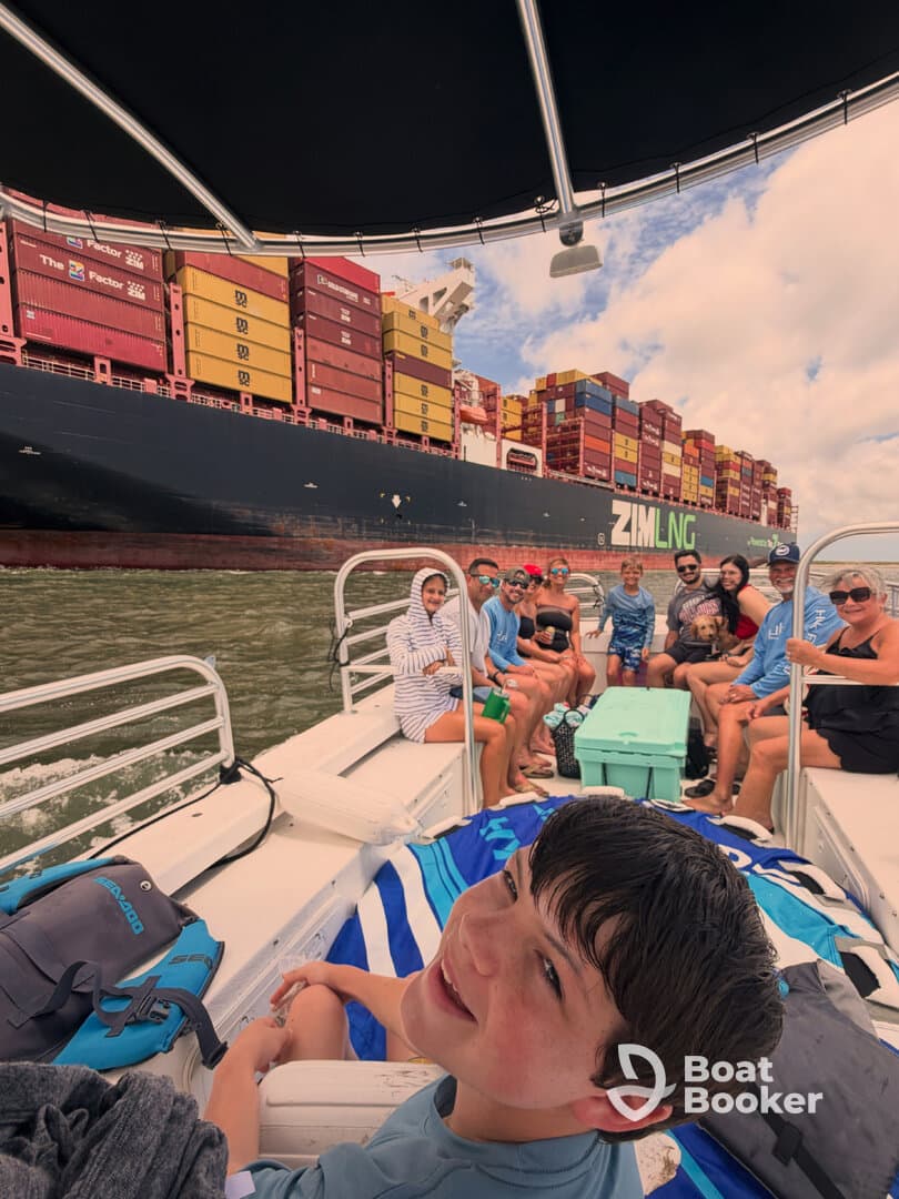 A lively group enjoys a boat trip alongside a massive container ship, capturing the excitement of family fun on the water.