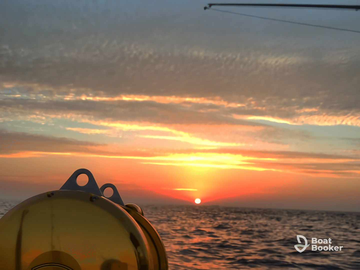 A stunning sunset view from a boat, showcasing the tranquil sea and a glimpse of the boat's equipment — perfect for capturing the serene beauty of evening cruises.