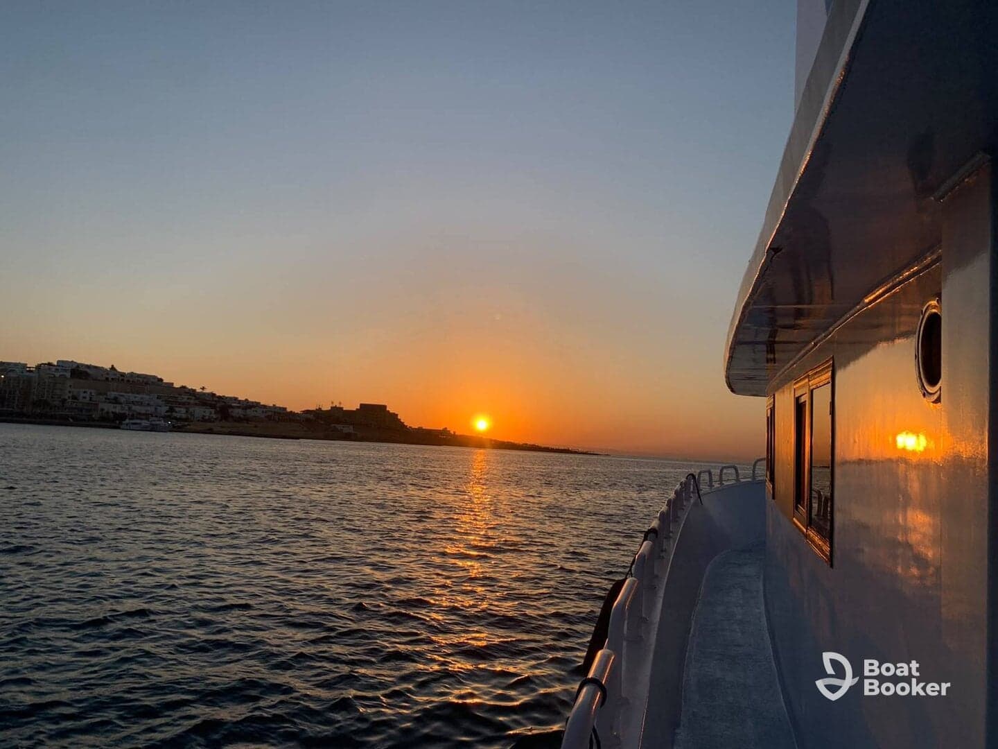 A serene sunset view from the deck of a boat, showcasing the tranquil waters and distant shoreline — perfect for evening cruises.