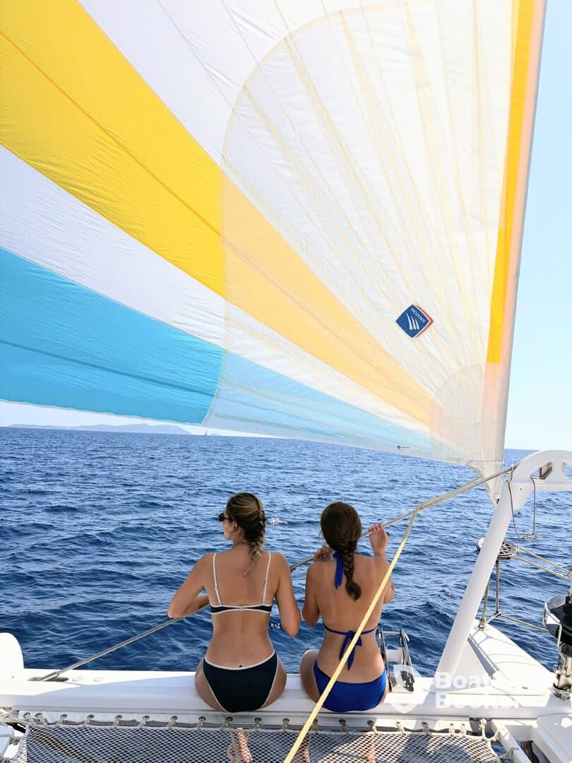 Two friends enjoy a sailing adventure on a catamaran, taking in the stunning ocean views while relaxing under the colorful sail.