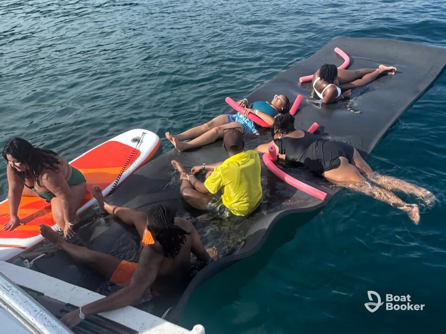 A lively group enjoys a day on the water, relaxing on a floating mat and paddleboarding, capturing the essence of summer fun and camaraderie.