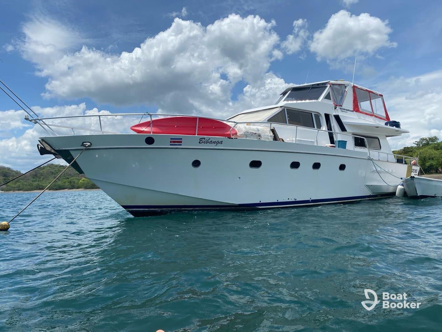A stunning yacht named 'Bilanga' docked in clear waters, showcasing its elegant design against a backdrop of fluffy clouds and lush greenery.