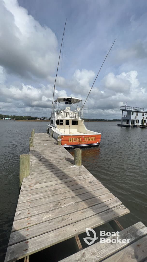 A striking view of the 'REEL TIME' yacht docked at a wooden pier, showcasing its sleek design against a cloudy sky — perfect for fishing trips or leisurely cruises.