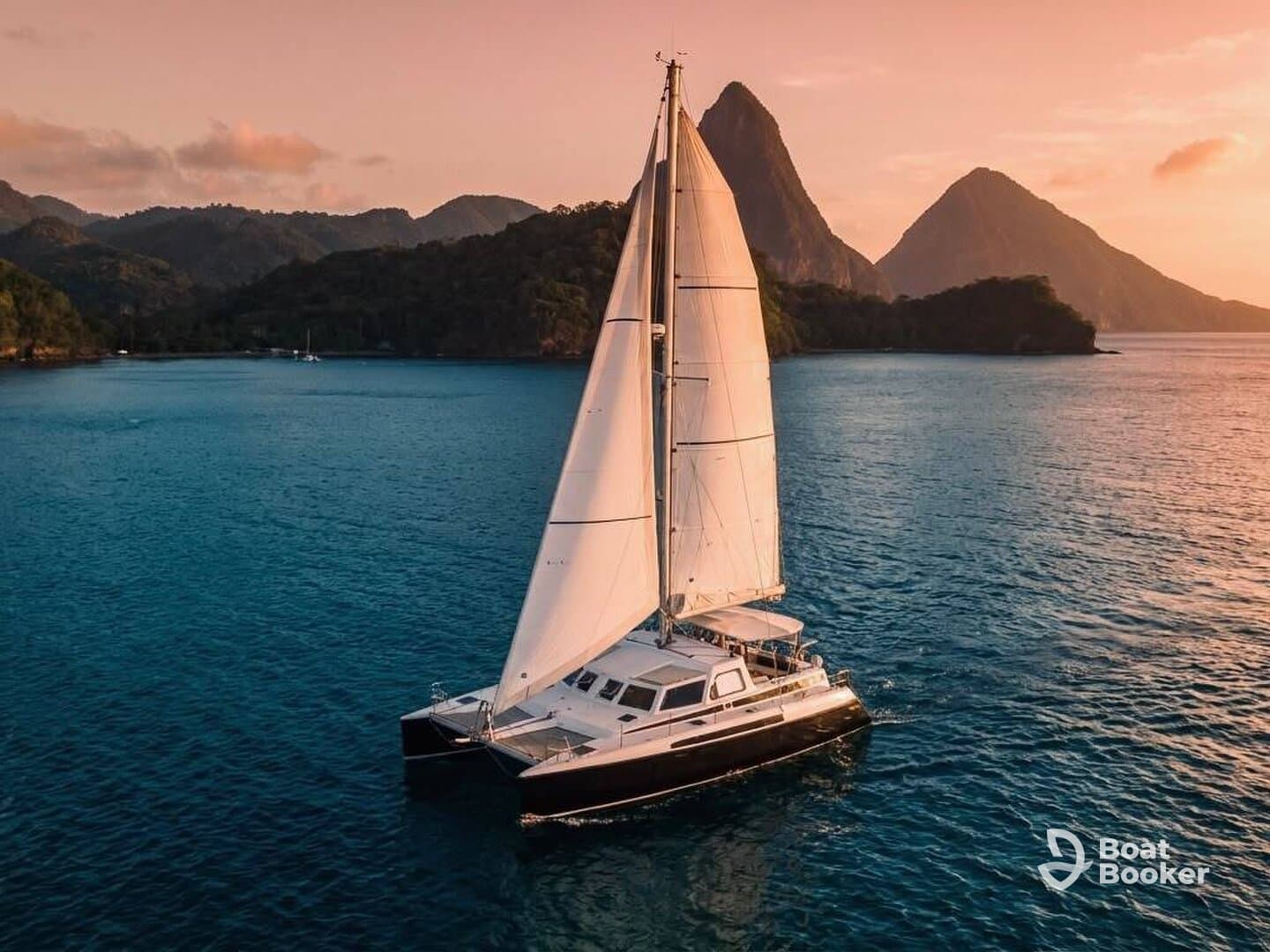 A stunning aerial view of a catamaran sailing in serene waters, framed by lush mountains — an ideal setting for sailing adventures and exploration.