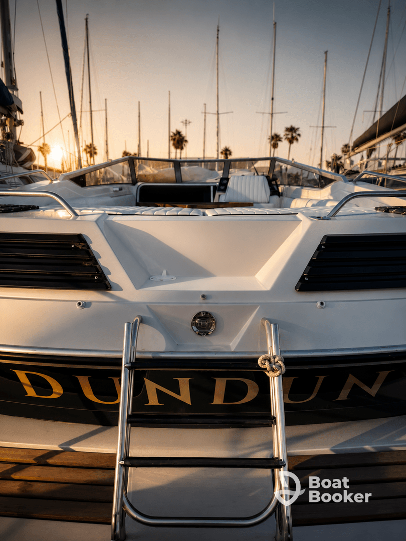 A stunning view of the back of a yacht named 'DUNDUN' docked at sunset, showcasing its sleek design against a backdrop of masts and palm trees.