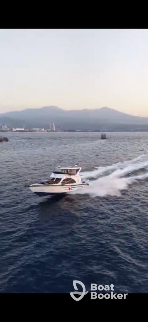An aerial view of a sleek speedboat cruising through open waters, showcasing its dynamic design against a backdrop of mountains.