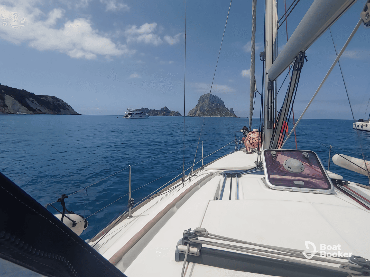 A scenic view from a sailboat with guests enjoying the ride, showcasing a stunning island backdrop and clear blue waters.