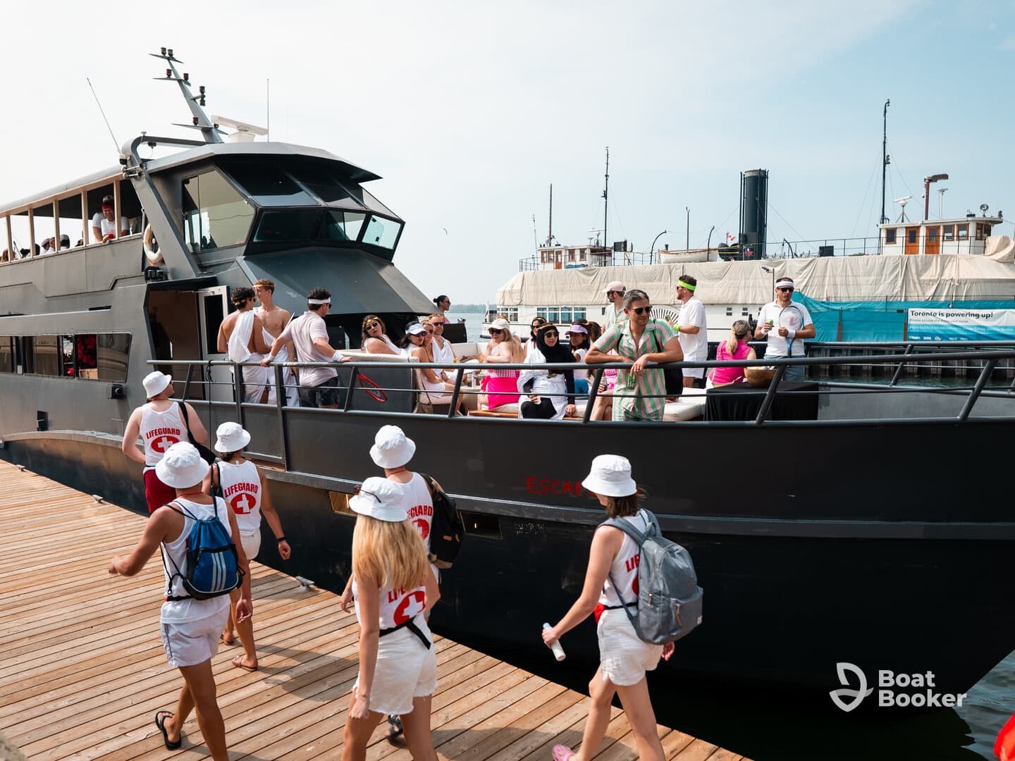 A lively group of guests, dressed in themed attire, boards a party boat at the dock, ready for a fun-filled day on the water.
