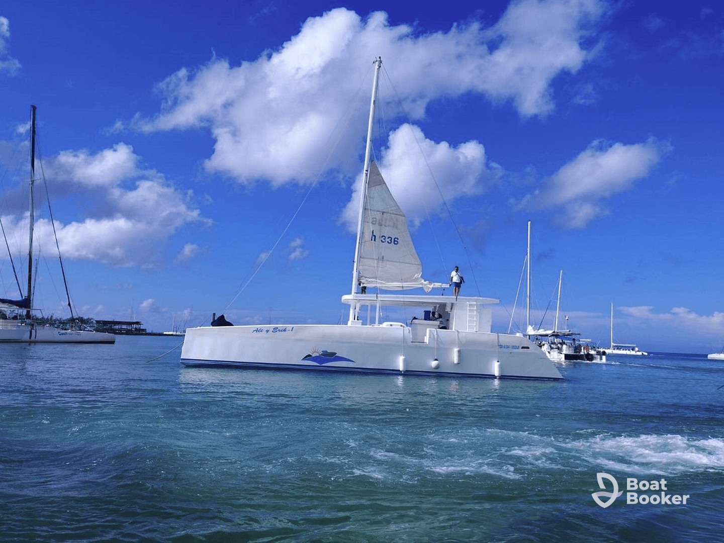 A sleek catamaran sails through clear waters, showcasing its elegant design against a backdrop of blue skies and nearby vessels — perfect for a day of adventure on the water.