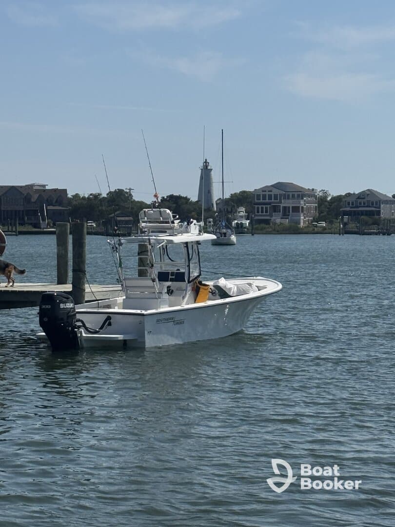 A sleek speedboat docked in calm waters, with a lighthouse and waterfront homes in the background, perfect for fishing or leisure outings.