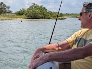 A man enjoys a serene boating experience while observing a bird in its natural habitat, showcasing the beauty of wildlife and nature during a day on the water.